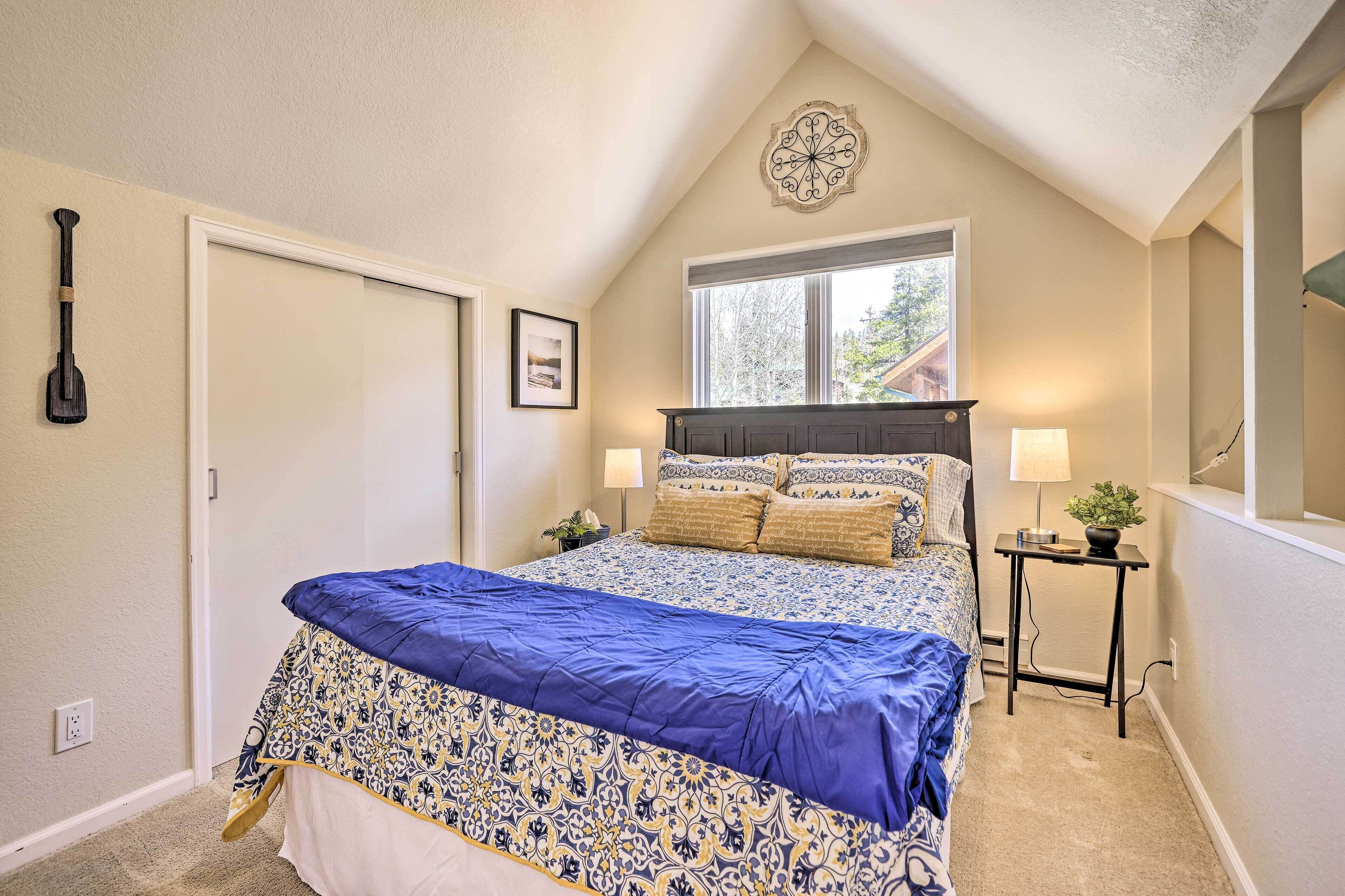 A bedroom with a bed, a window, a nightstand, a lamp, and a wall decoration.