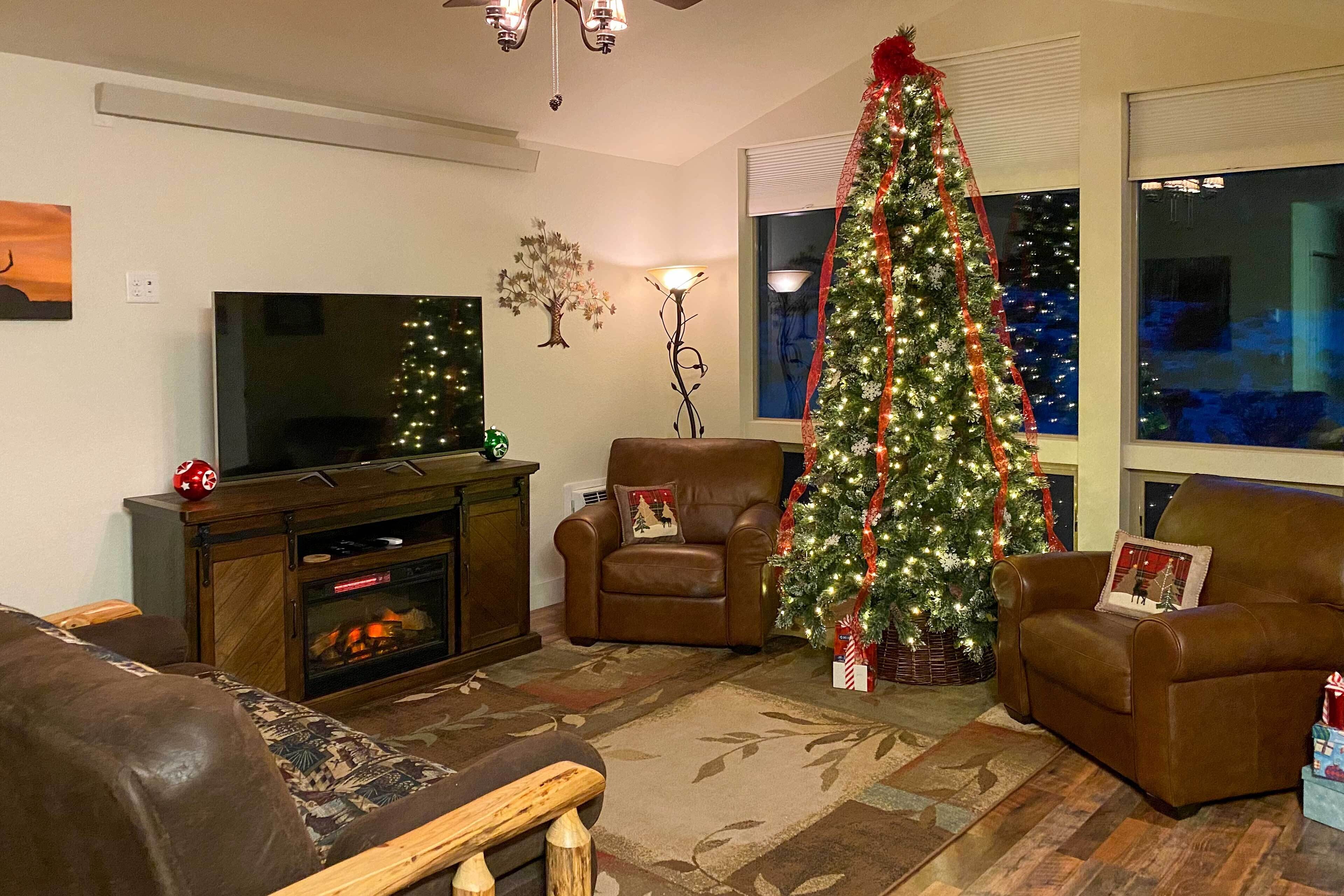 A living room with a fireplace, a television, a Christmas tree, and two armchairs.