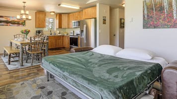 Une chambre avec un lit, un coin repas avec une table et des chaises, une cuisine avec des meubles en bois et des appareils électroménagers, et un couloir avec une porte.