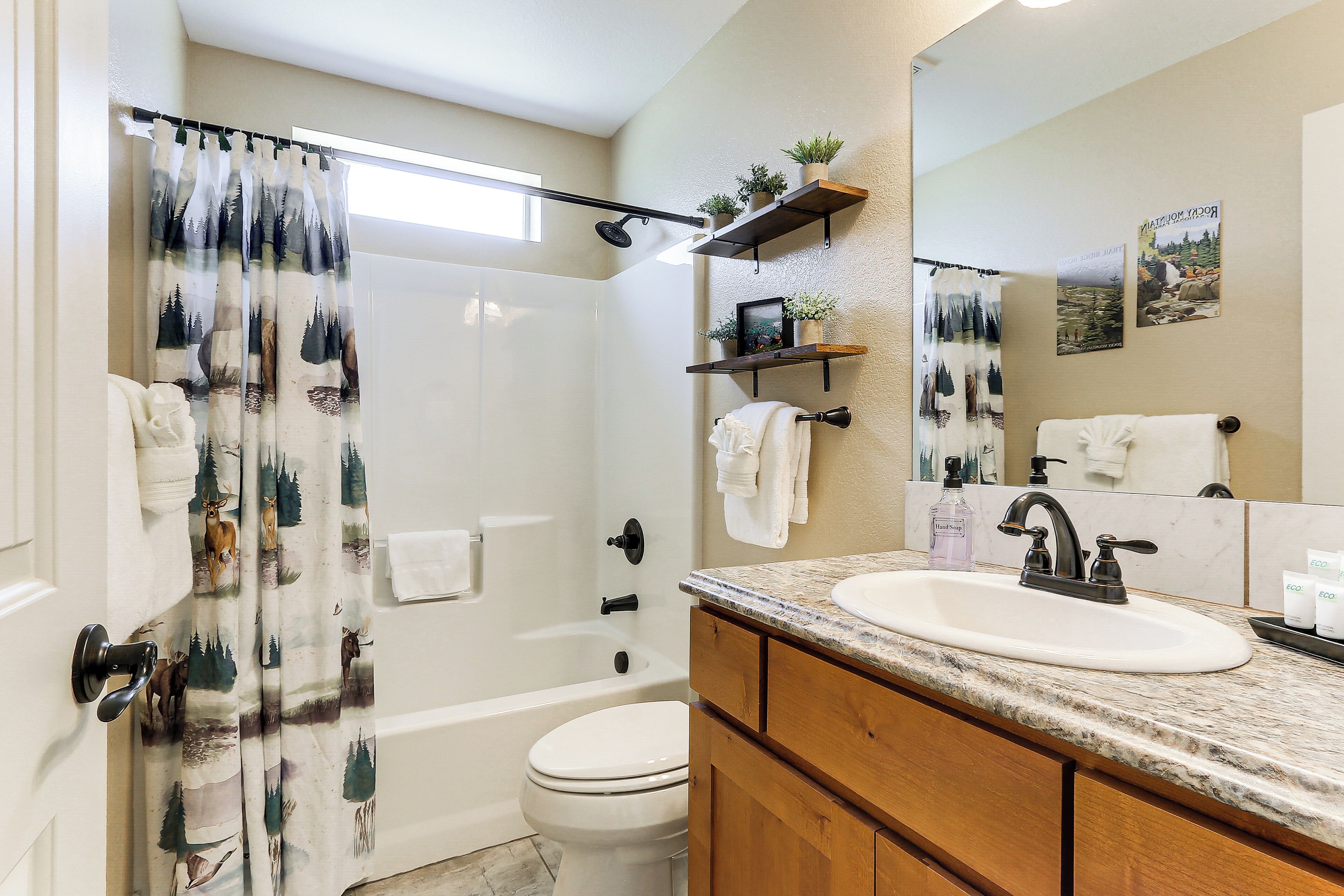 Un baño con cortina de ducha, un inodoro, un lavabo con espejo y una repisa con plantas.