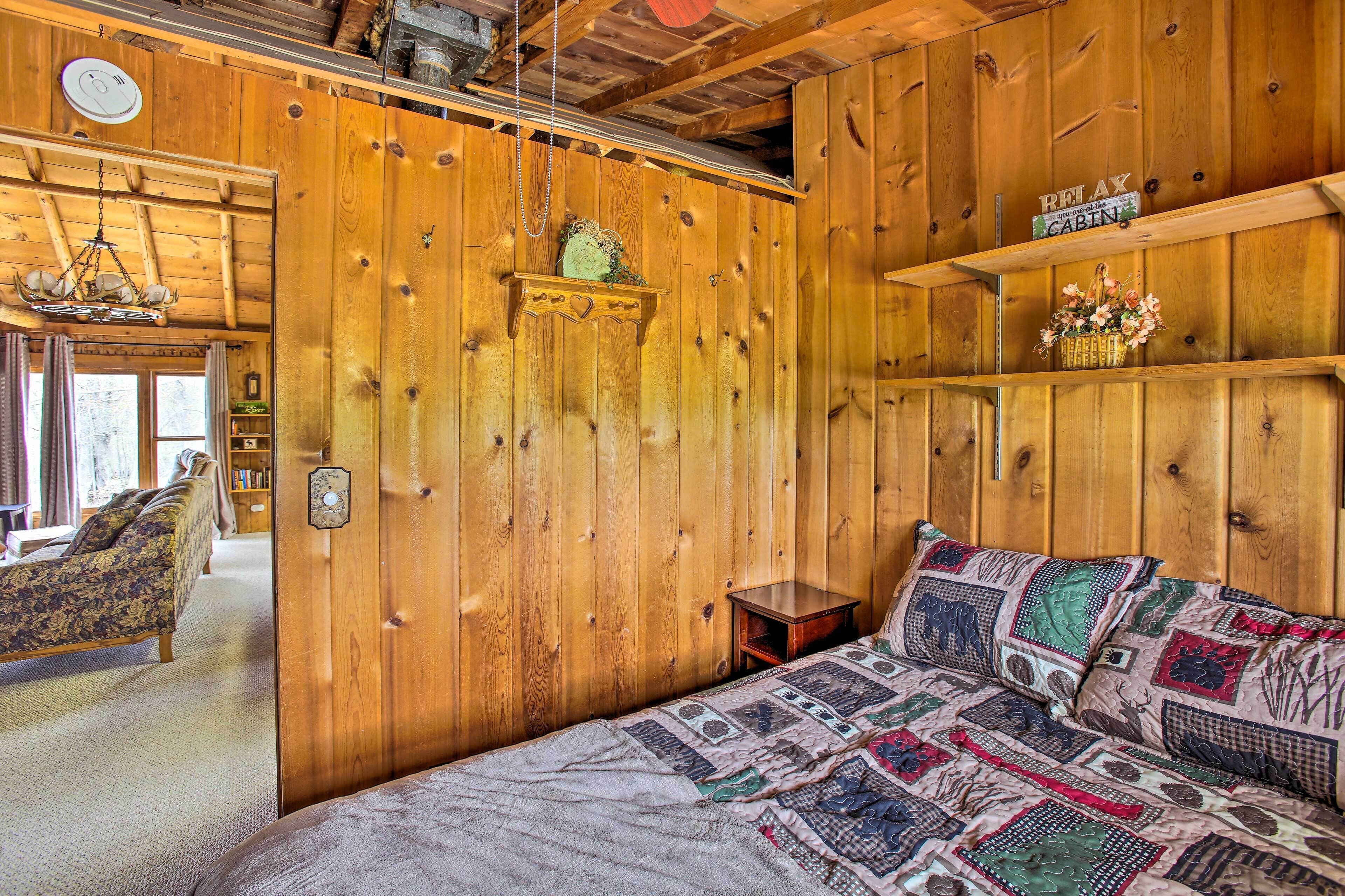 A cozy cabin-style room with wooden walls, a bed with a quilt, a small table, and a bookshelf.