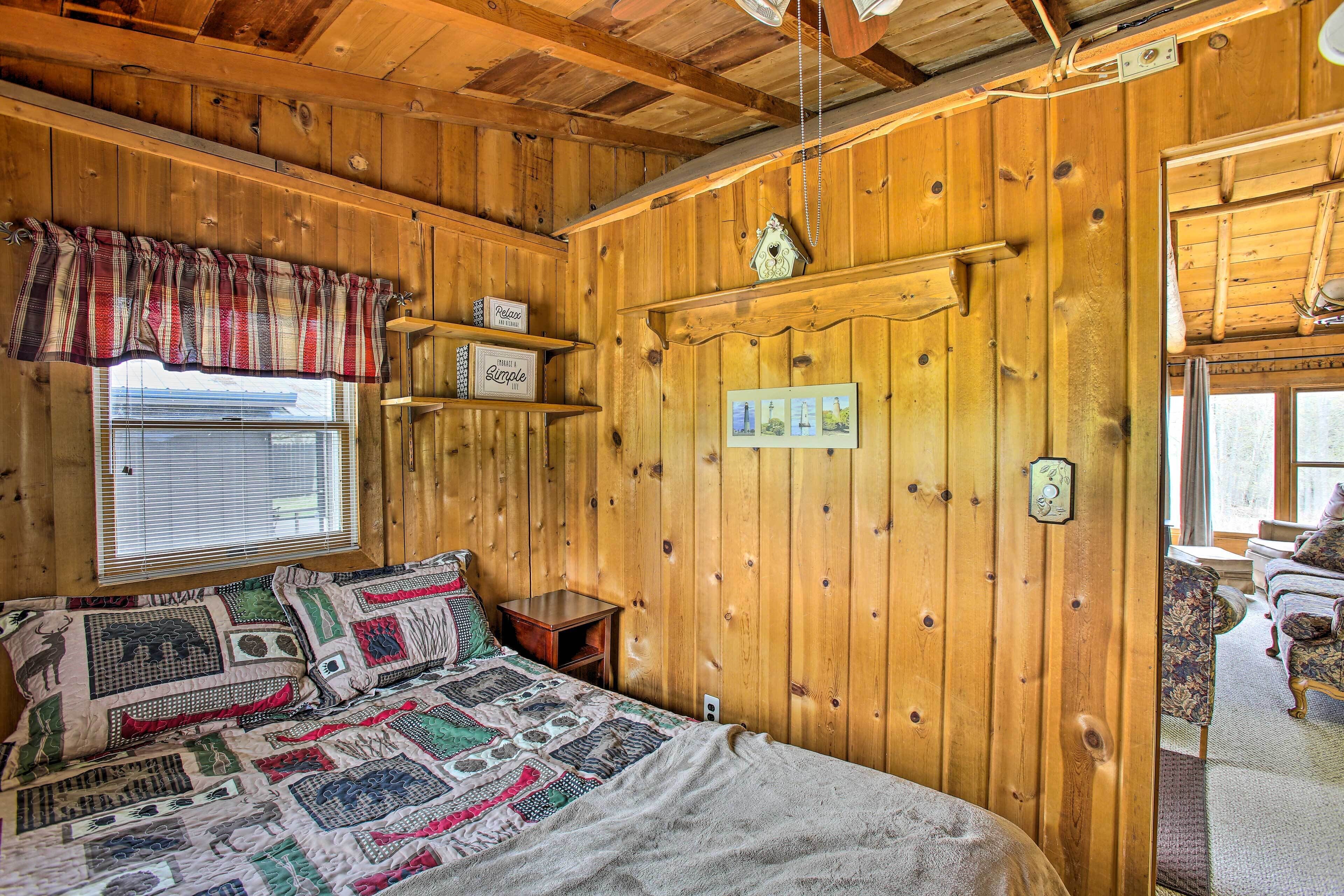 Ein gemütlicher Holzraum mit einem Bett, einem Fenster mit Jalousien, einem Regal mit Dekoration und einer Tür mit Lichtschalter.