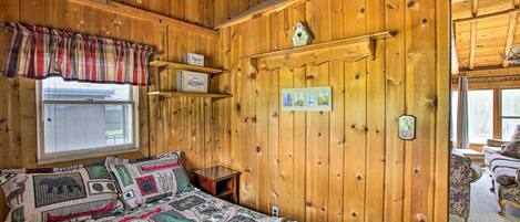 Ein gemütlicher Holzraum mit einem Bett, einem Fenster mit Jalousien, einem Regal mit Dekoration und einer Tür mit Lichtschalter.
