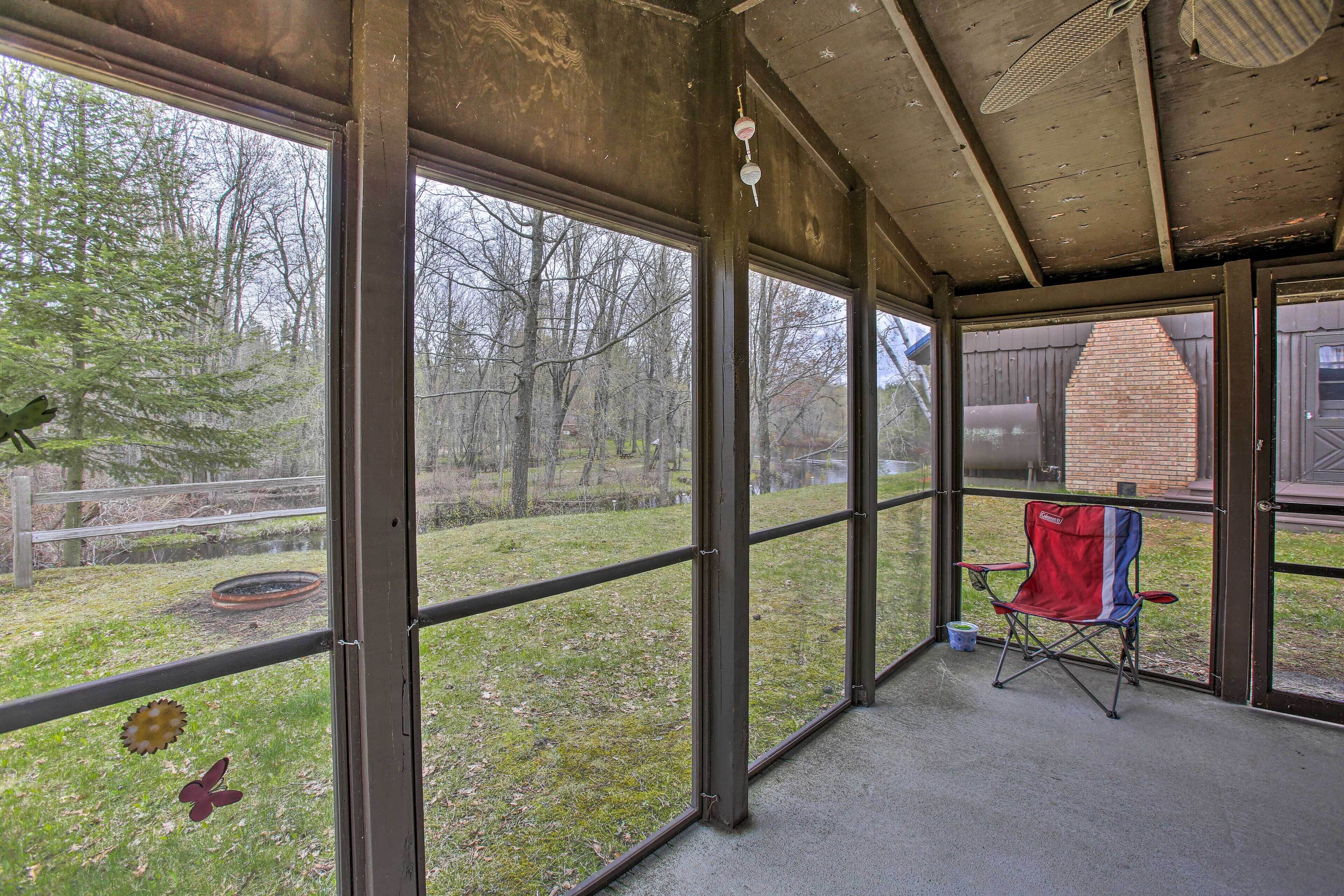 A covered porch with large windows, a red folding chair, and a small bucket.
