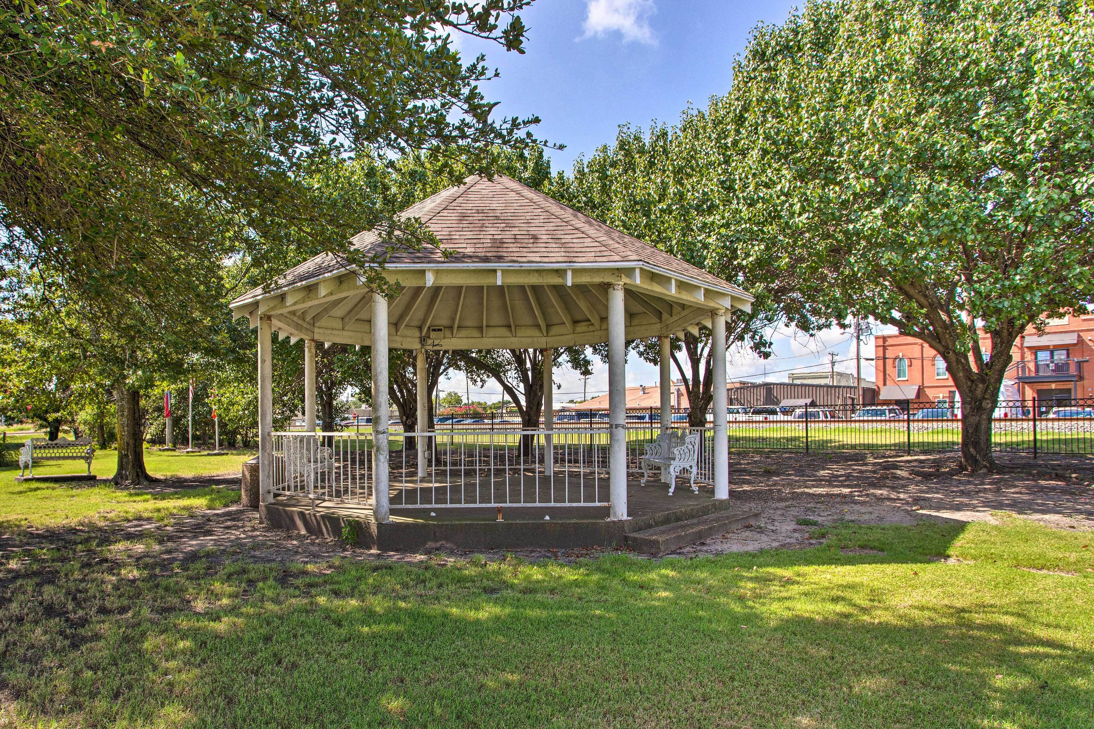 Ein Gazebo in einem Park mit Rasenflächen, Bänken und Bäumen.