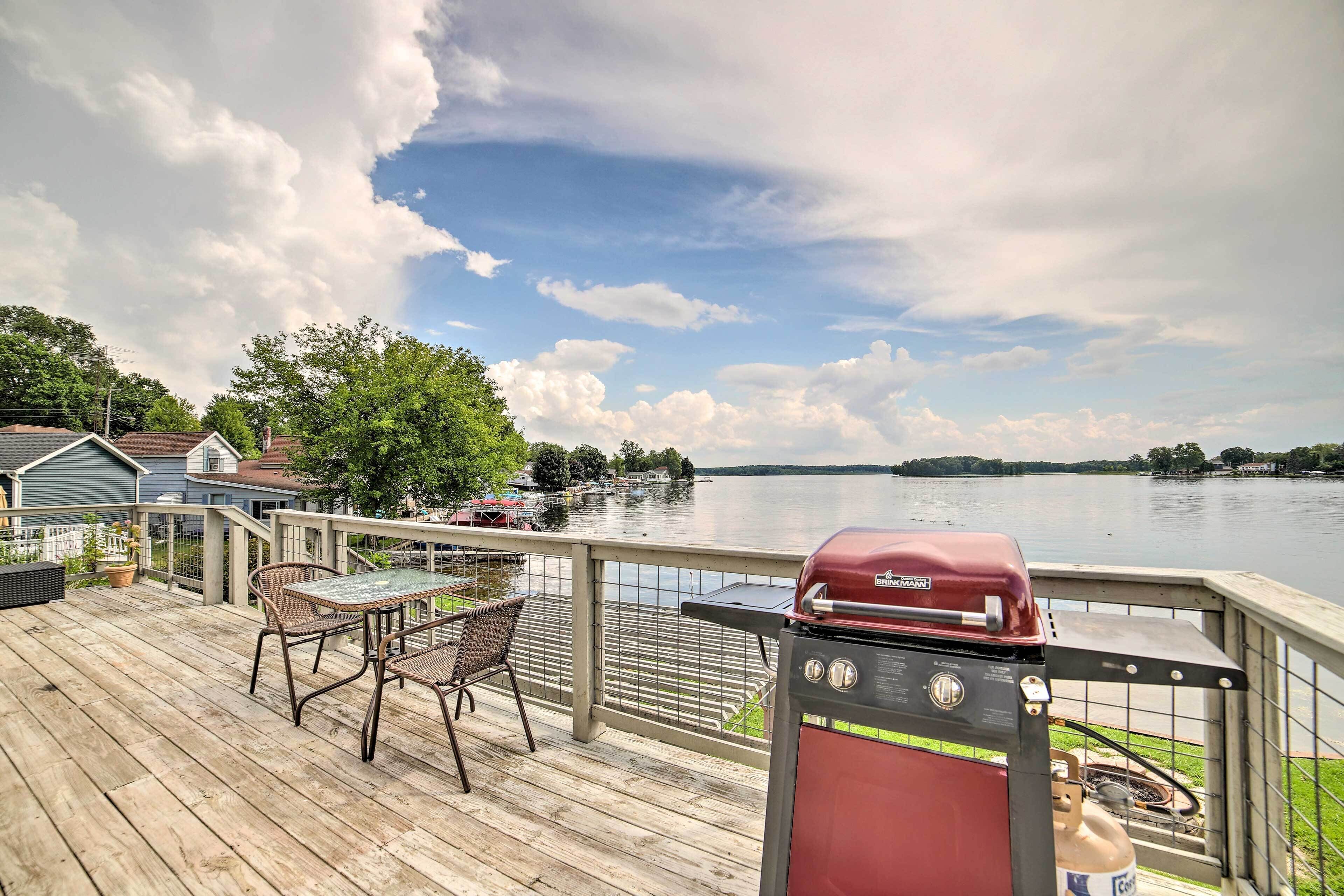 A deck with a grill and chairs overlooking a lake.