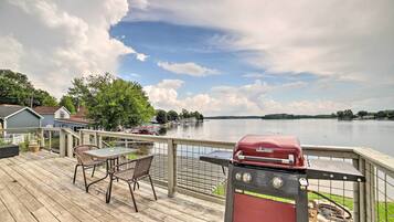 A deck with a grill and chairs overlooking a lake.