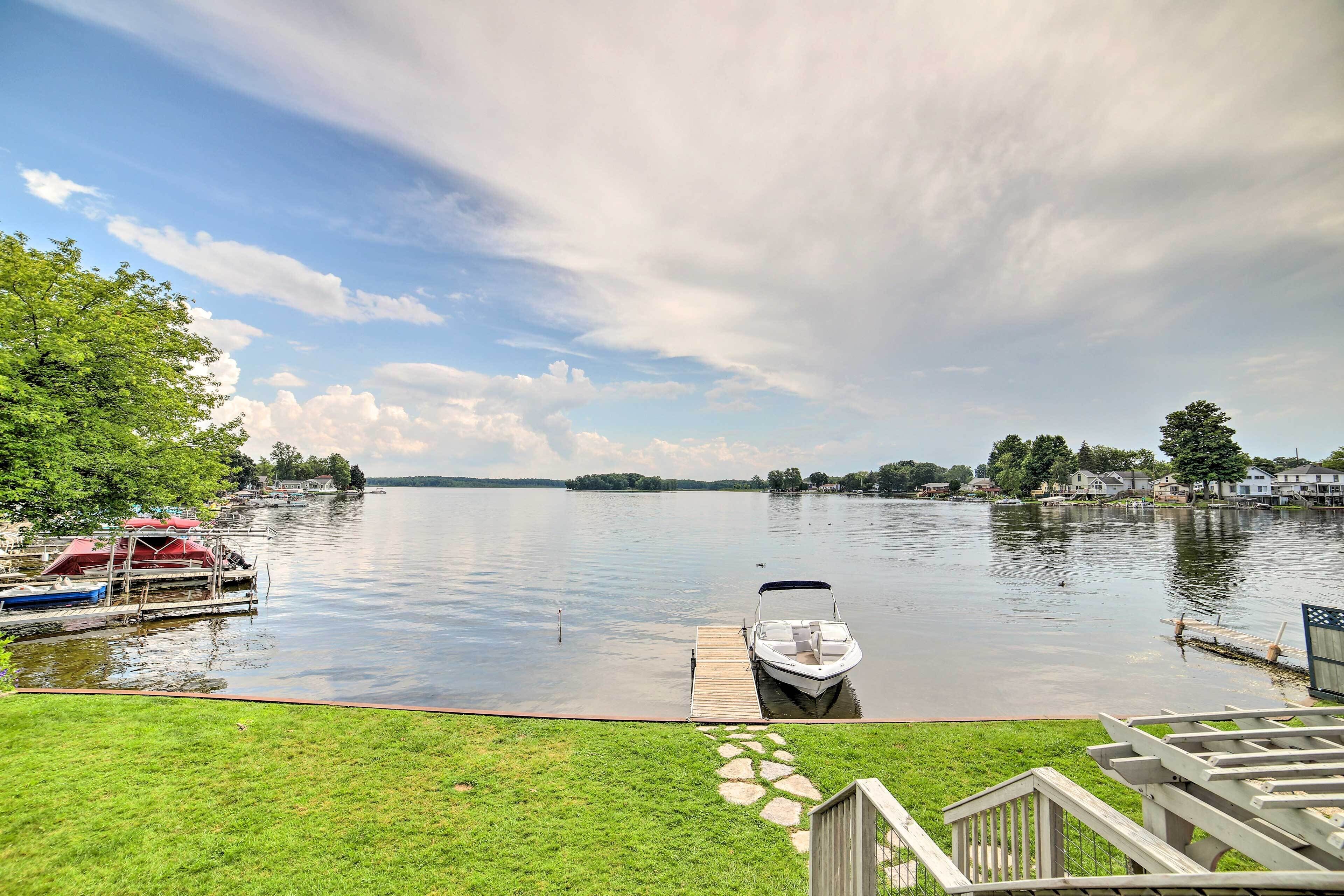 A lake with a dock and a boat, surrounded by greenery and houses.