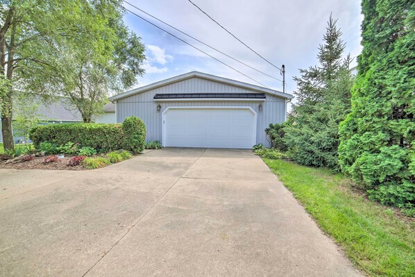 A single-story building with a white garage door, surrounded by greenery and a clear sky. - Waterfront Michigan Center Home w/ Boat Dock! (Michigan Center)