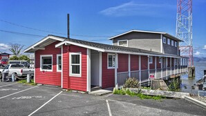 A red building with a dock extending into the water, a parking lot, and a red and white tower in the background. - Waterfront Condo on Pier in Downtown Astoria! (Astoria)