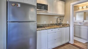 A modern kitchen with white cabinets, a stainless steel refrigerator, a microwave, and a granite countertop. - Waterfront Condo on Pier in Downtown Astoria! (Astoria)