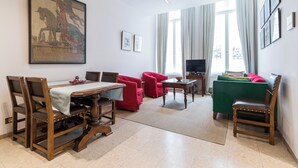 A living room with a dining table, red chairs, a green sofa, and a television. - Room of Puebla (Brugge)