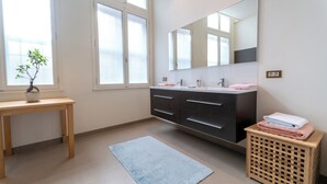 A modern bathroom with a wooden vanity, a large mirror, and a small potted plant. - Room of Puebla (Brugge)
