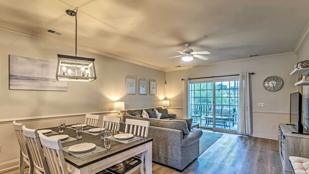 A dining area with a table set for four, a gray sofa, and a ceiling fan. - 3 Mi to Myrtle Beach: Coastal Condo w/ Pool! (Myrtle Beach)