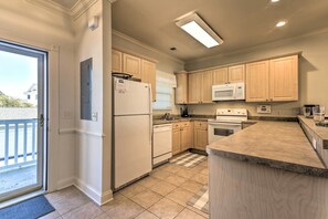 A modern kitchen with light wood cabinets, a white refrigerator, a microwave, and a stove.