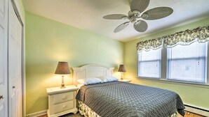 Ein Schlafzimmer mit Bett, Nachttischen, Lampen, Deckenventilator und einem Fenster mit Jalousien.