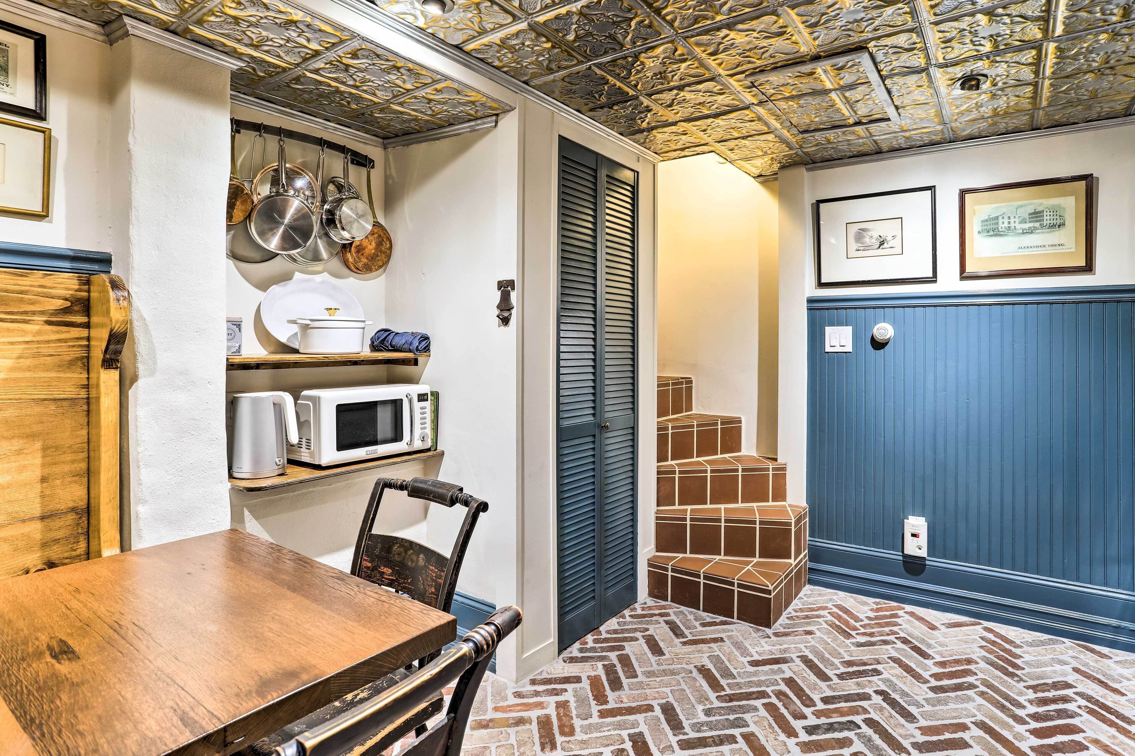A kitchen with a wooden table, chairs, a microwave, and hanging pots.