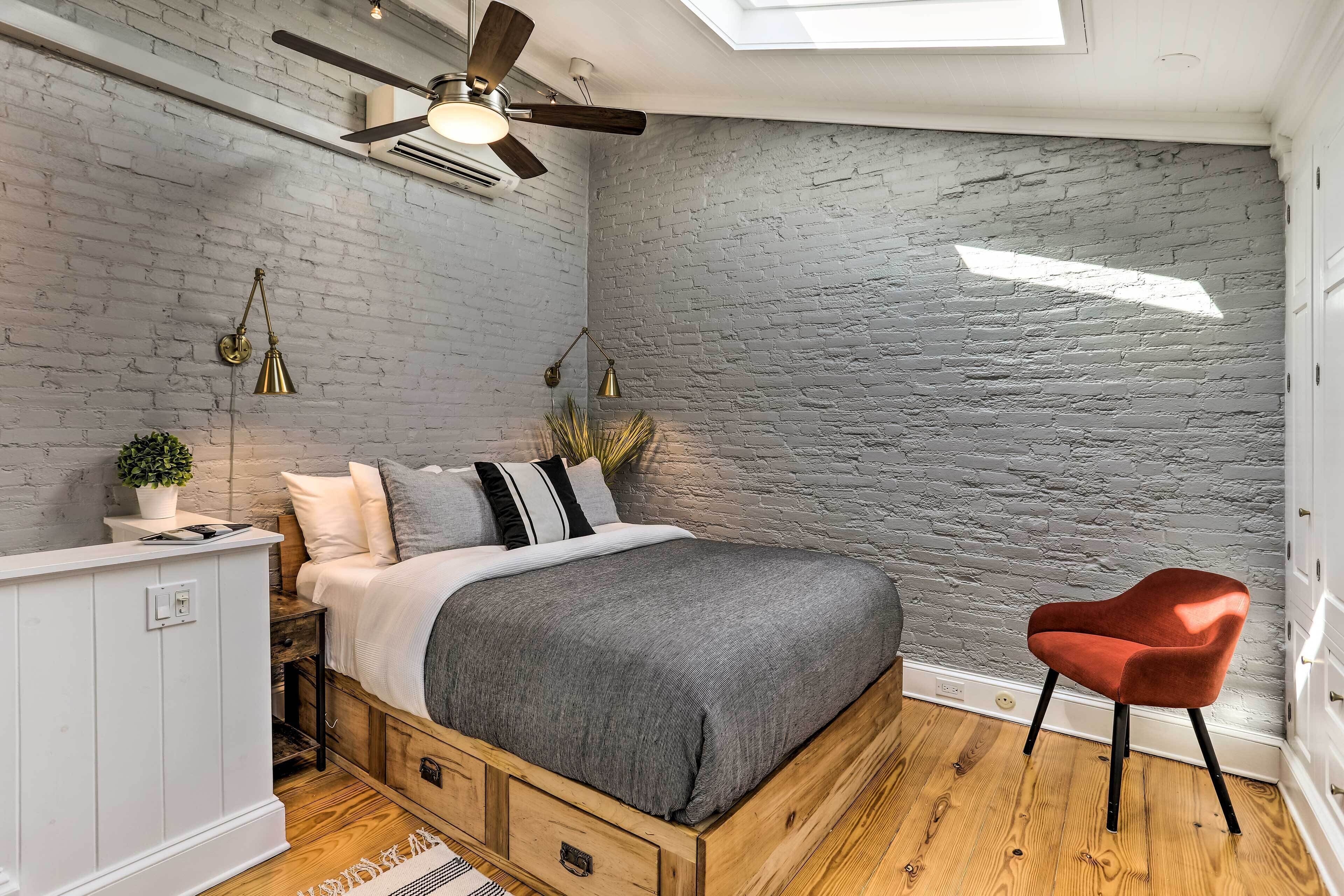A bedroom with a bed, a red chair, a ceiling fan, and a skylight.