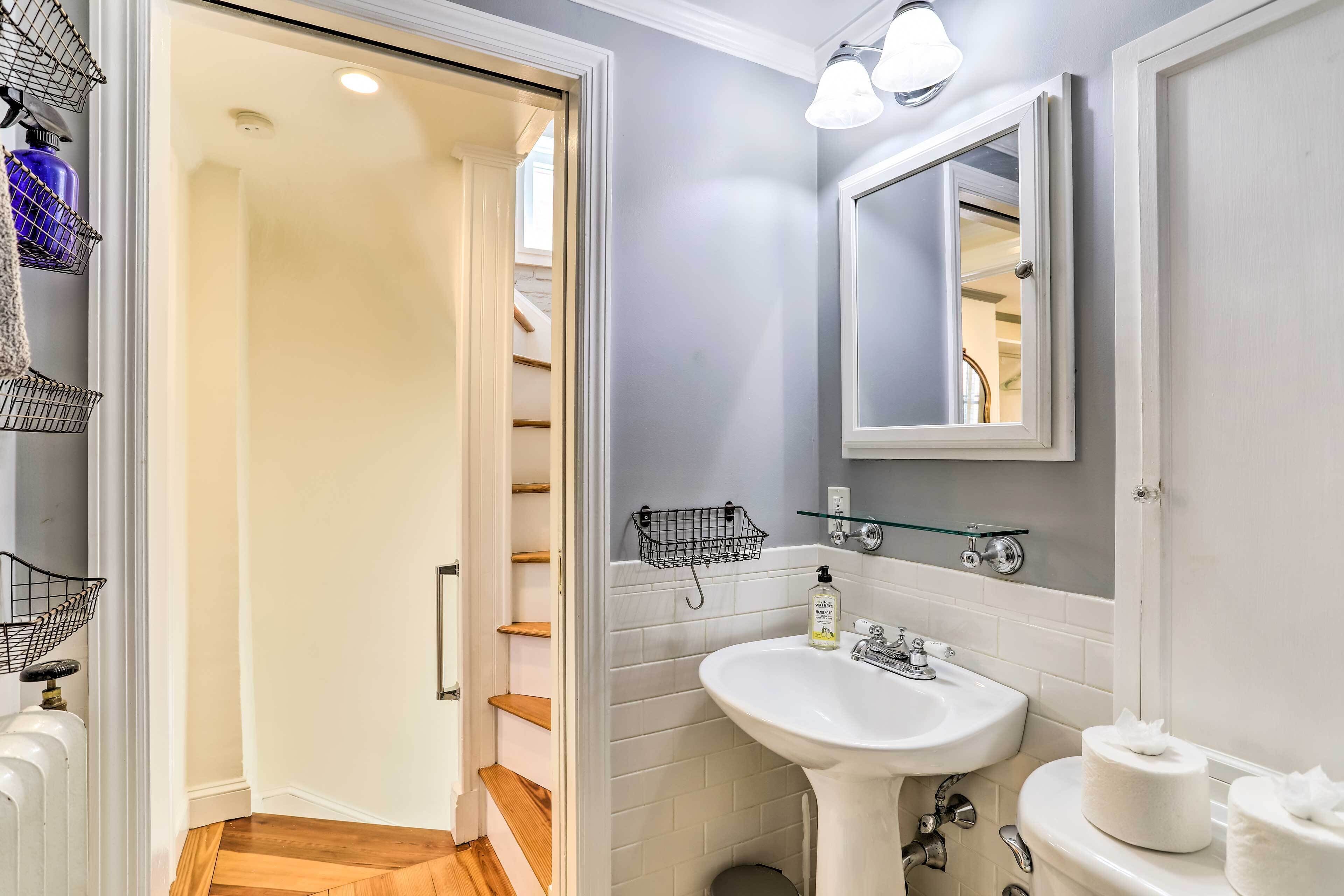 A bathroom with a white sink, a mirror, and a toilet. There is a towel rack and a glass shelf above the sink.