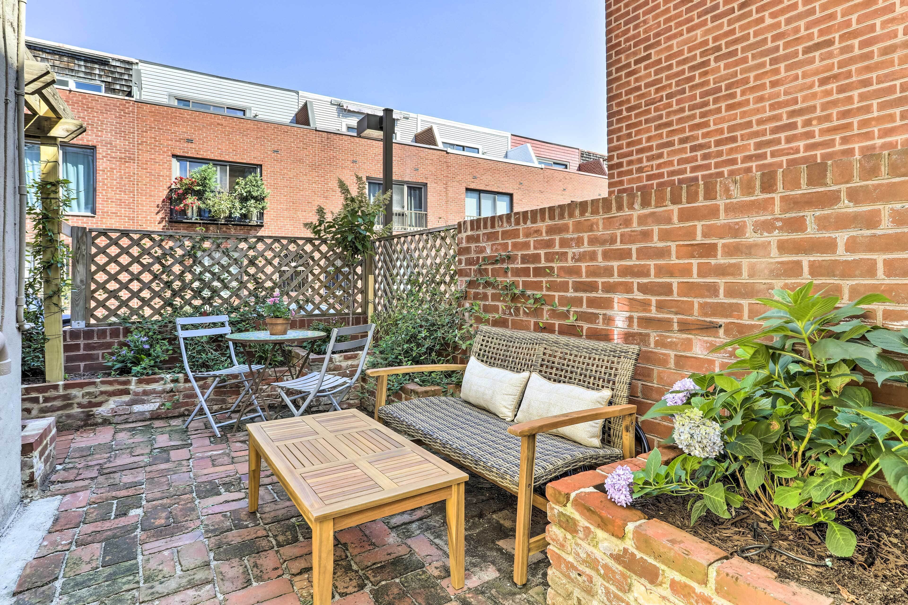 A patio with a wooden table, a wicker sofa, and a small garden area with plants.