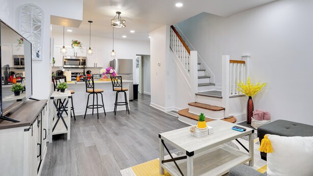 A modern kitchen with white cabinets, a dining area with a white table and chairs, and a staircase leading to an upper floor. - Philly Hub Near Intl Soccer, Downtown Attractions (Philadelphia)