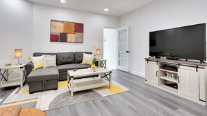A modern living room with a grey sofa, a coffee table, a flat-screen TV, and a cabinet with shelves. - Philly Hub Near Intl Soccer, Downtown Attractions (Philadelphia)
