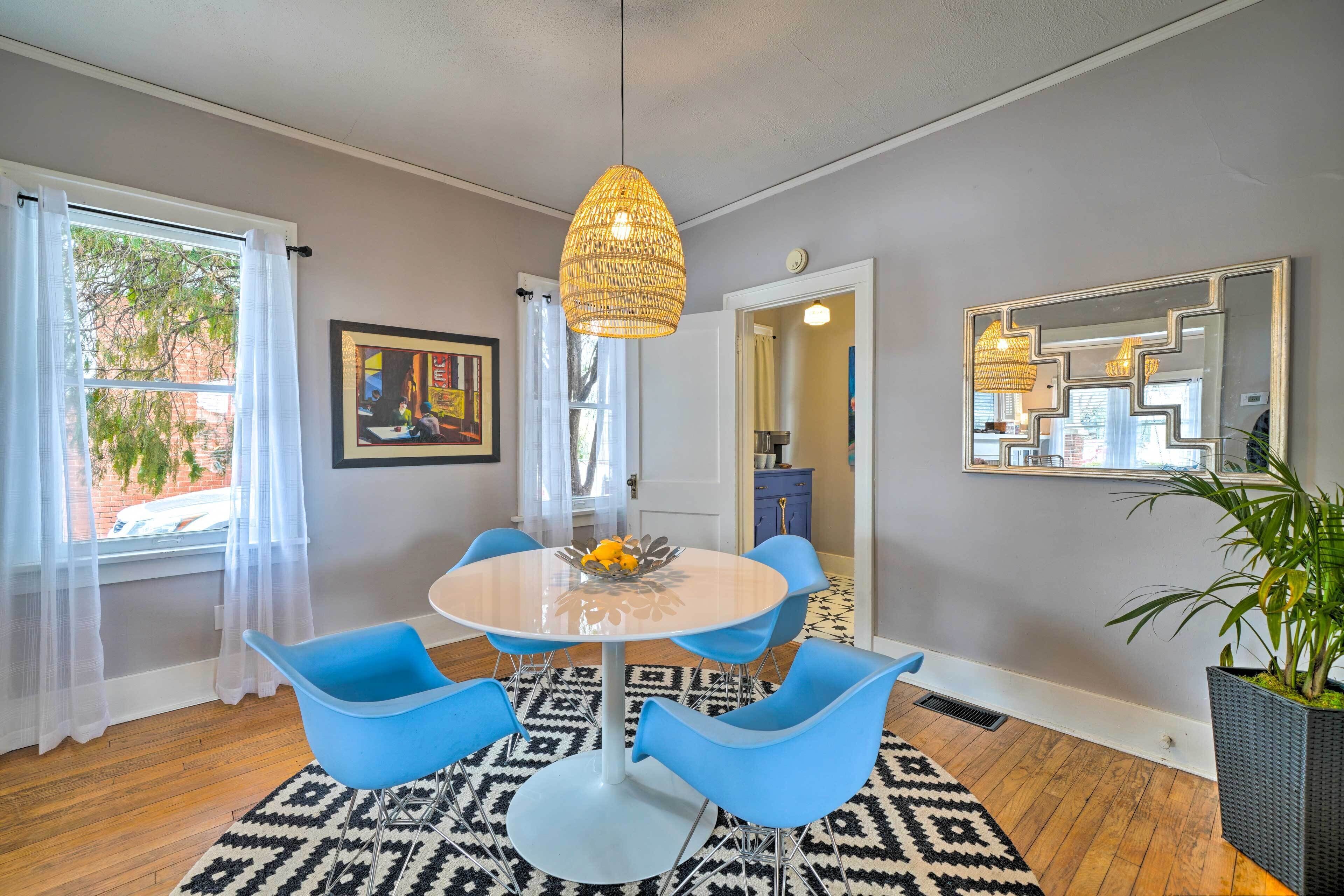 A dining area with a round table, blue chairs, a hanging light fixture, and a patterned rug.