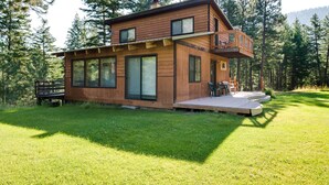 A modern wooden cabin with a deck, large windows, and a view of the surrounding forest. - Conconully Cabin on 42 Private Acres Near Hiking! (Conconully)