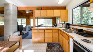 A compact kitchen with wooden cabinets, a built-in stove, and a large window. - Conconully Cabin on 42 Private Acres Near Hiking! (Conconully)