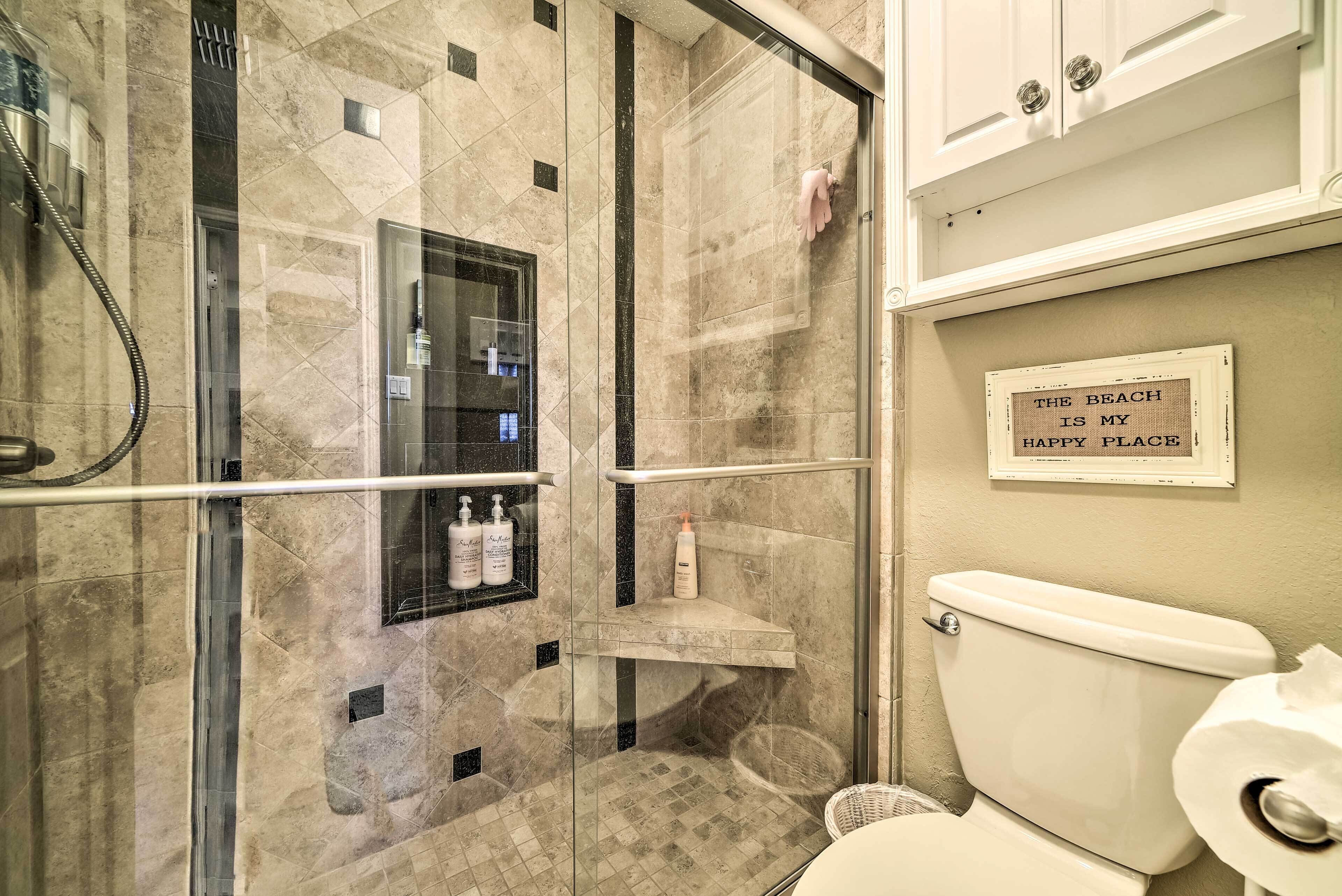 Une salle de bain avec une douche à parois de verre, des toilettes et une étagère contenant des articles de toilette.