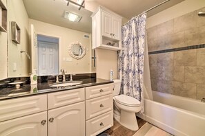 A bathroom with a white vanity, a toilet, a bathtub, and a shower curtain.