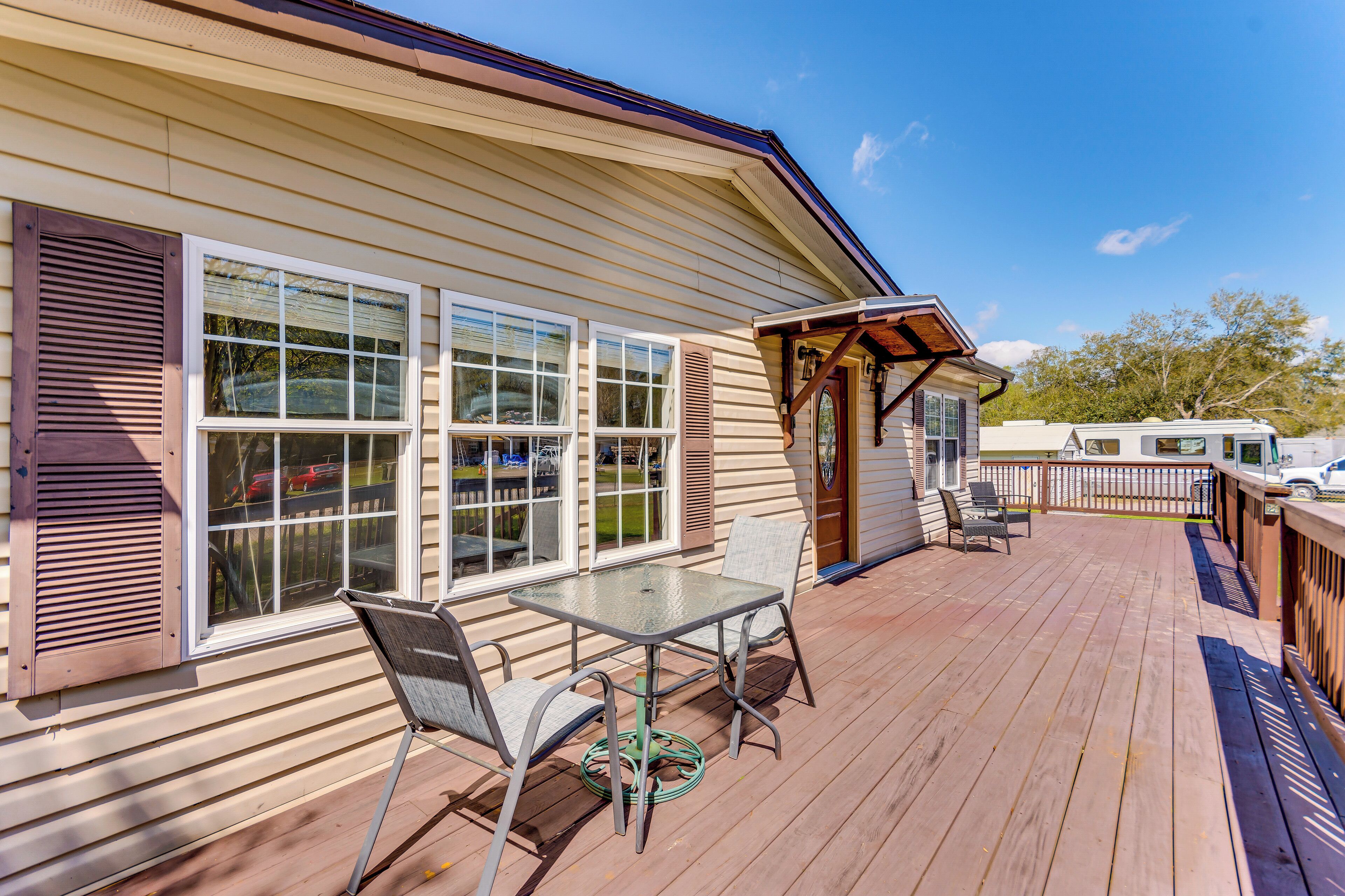 A wooden deck with a glass table and chairs, a covered seating area, and a view of a vehicle in the background.