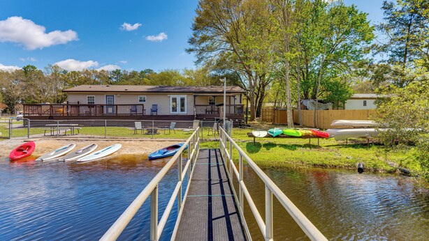 A wooden dock leading to a calm body of water with kayaks and a paddleboard.