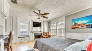 A bedroom with a bed, a desk, a chair, a fireplace, and a cityscape painting on the wall.