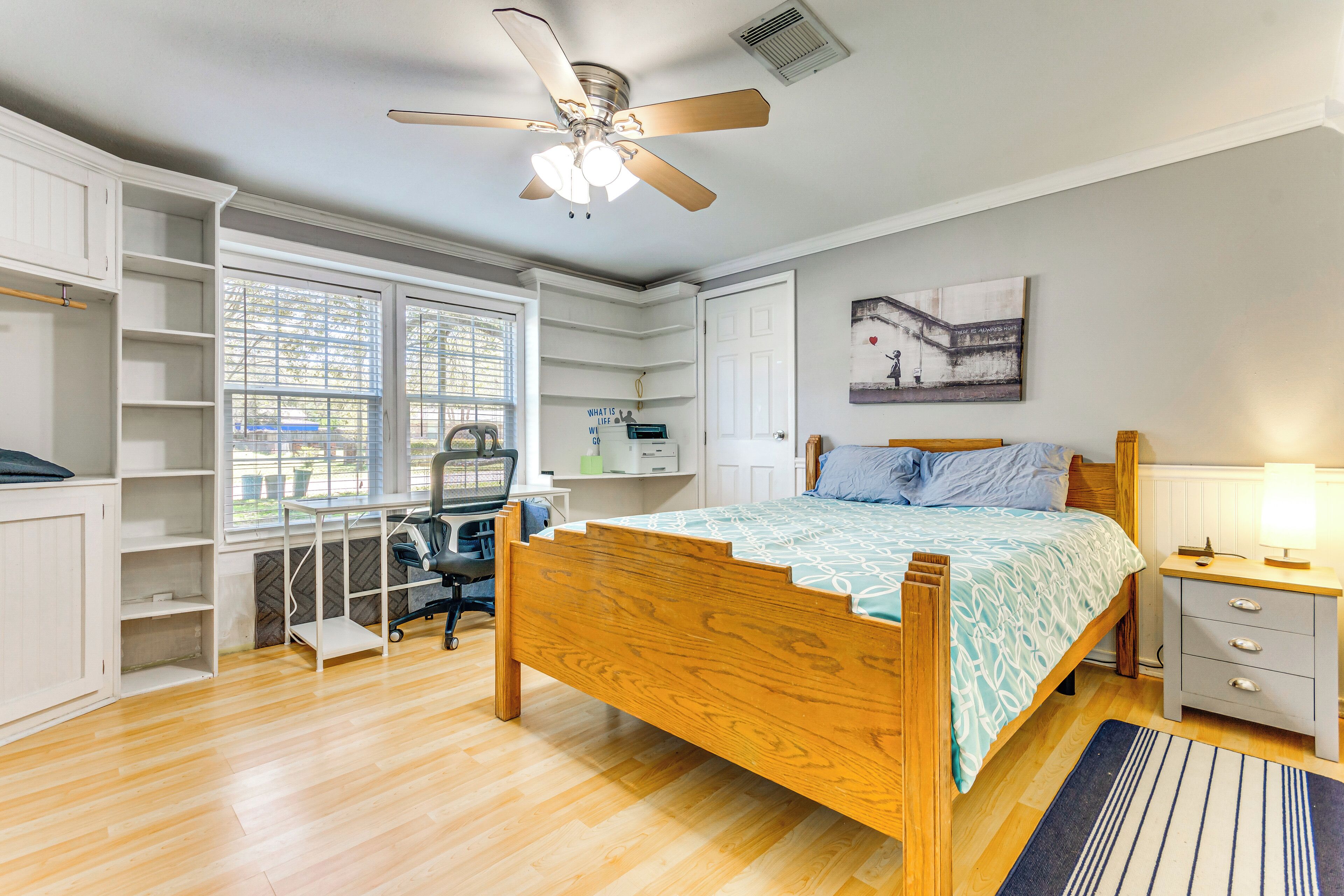 Une chambre à coucher avec un lit en bois, un bureau avec une chaise, un ventilateur de plafond et des étagères intégrées.
