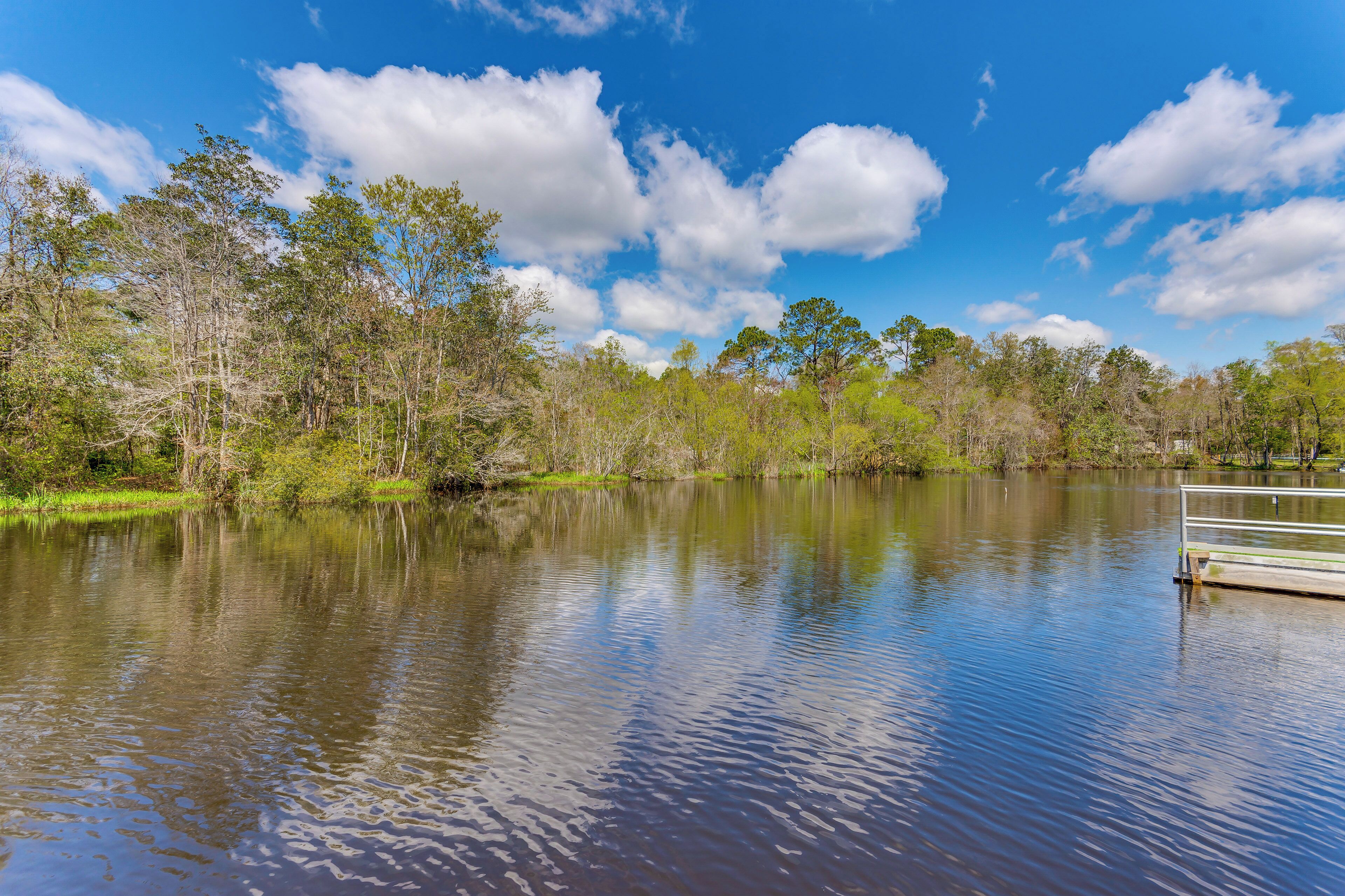 A calm lake with a dock extending into the water, surrounded by trees and a clear sky.