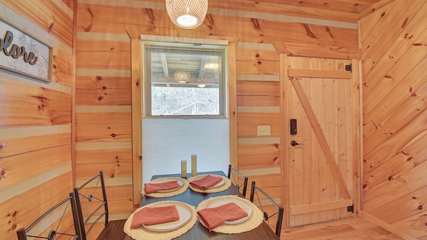 A wooden interior with a dining table set for four, a window with blinds, and a door. - Pet-friendly Cabin w/ Hot Tub in Daniel Boone NF (Beattyville)