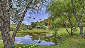 A rope bridge over a pond with trees on either side and a house in the background. - Pet-friendly Cabin w/ Hot Tub in Daniel Boone NF (Beattyville)
