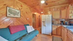 A wooden cabin interior with a kitchenette, a green sofa with a red blanket, and a ceiling fan. - Pet-friendly Cabin w/ Hot Tub in Daniel Boone NF (Beattyville)