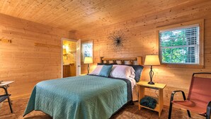 Une chambre dans une cabane en bois, avec un lit, des tables de chevet, une chaise et une fenêtre avec des stores.