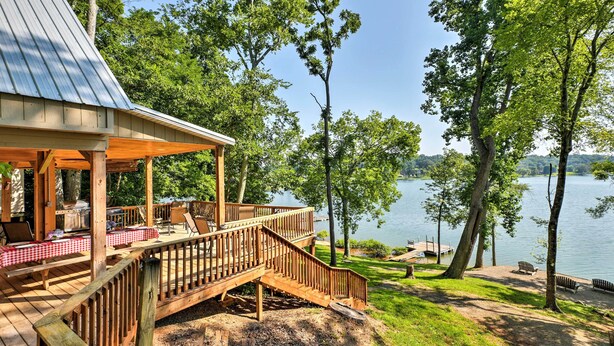 Une terrasse en bois avec un espace salon couvert, un barbecue et une vue sur le lac.