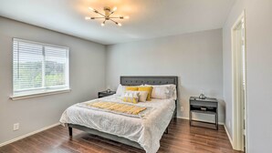 A bedroom with a bed, nightstands, a ceiling light fixture, a window with blinds, and a door. - Spacious + Sunny Austin Home ~ 12 Mi to Dtwn! (Austin)