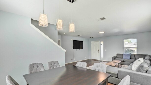 A modern living room with a dark wooden dining table, grey upholstered chairs, a grey sofa, and hanging pendant lights. - Spacious + Sunny Austin Home ~ 12 Mi to Dtwn! (Austin)