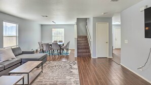 A modern living room with a sectional sofa, a coffee table, and a dining area with a table and chairs. A staircase leads to another room. - Spacious + Sunny Austin Home ~ 12 Mi to Dtwn! (Austin)