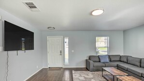 A modern living room with a sectional sofa, a flat-screen TV mounted on the wall, and hardwood flooring. - Spacious + Sunny Austin Home ~ 12 Mi to Dtwn! (Austin)