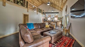 Un'ampia zona giorno con un divano modulare in pelle marrone, un tappeto rosso con motivi decorativi e un soffitto in legno.
