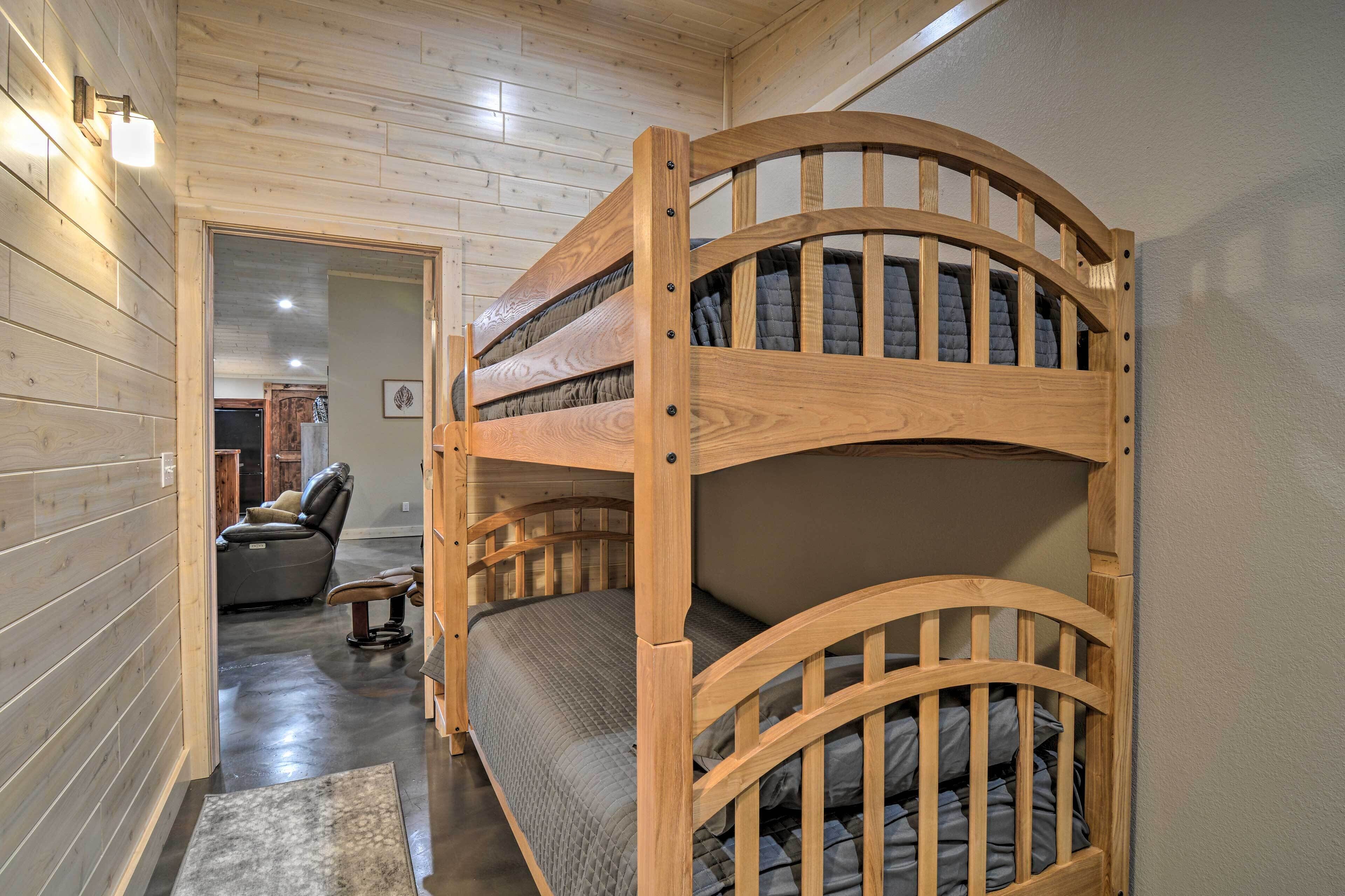Uma cama beliche com estrutura de madeira e colchão acolchoado, uma poltrona de couro e uma pequena mesa em um quarto com paredes de madeira e piso encerado.