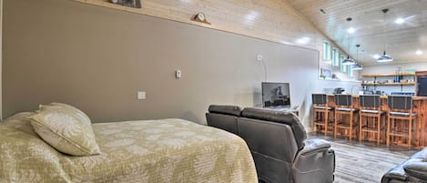 Una habitación con cama, una butaca reclinable, televisor y una zona de cocina con taburetes de bar.