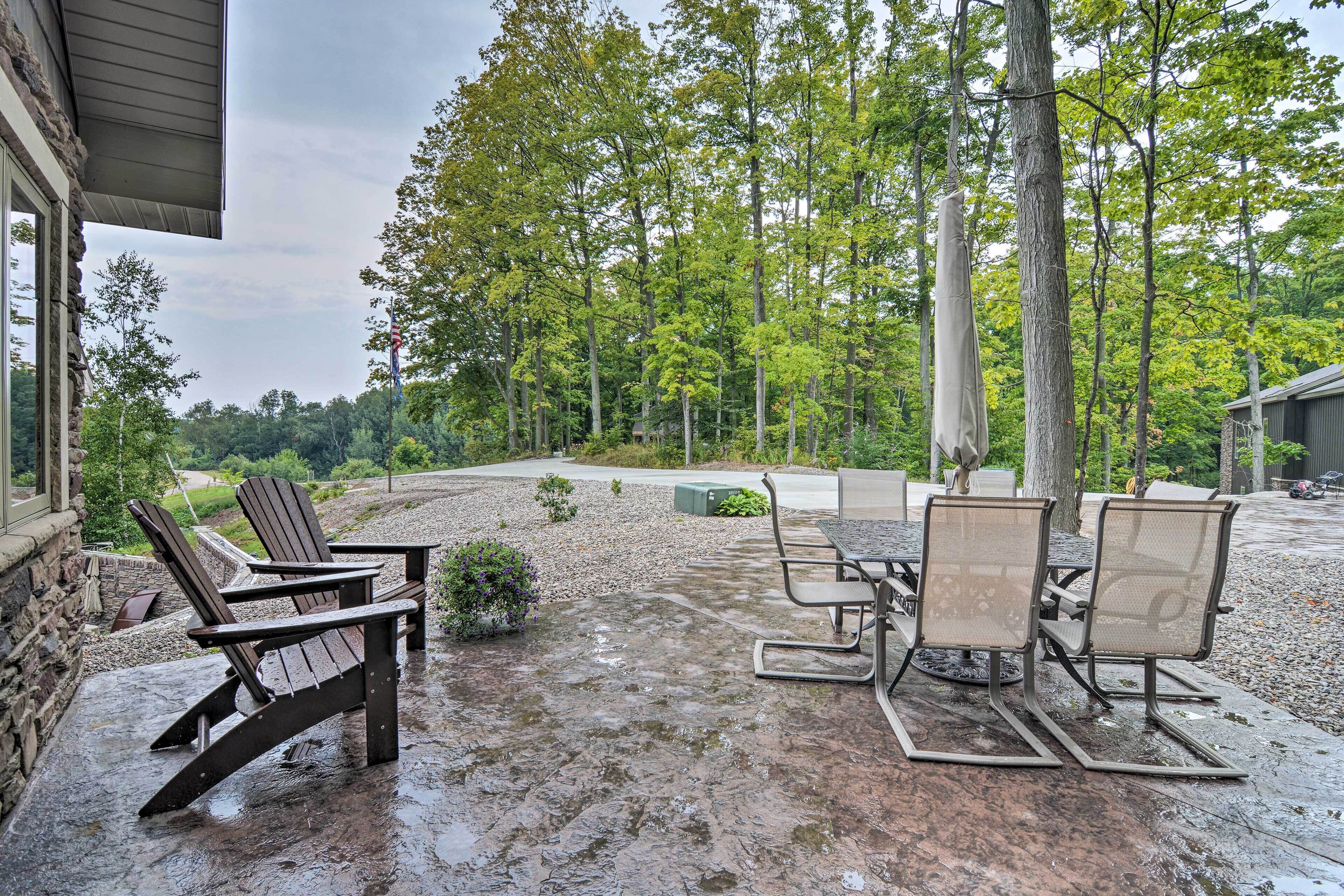 Une terrasse extérieure avec des fauteuils Adirondack et une table, entourée d’arbres et d’un mur de pierres.