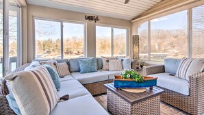 A sunlit room with a large sectional sofa, a coffee table with a decorative bowl, and a view of trees through large windows. - Private Boat Dock: Bright Lake Ozark Home! (Lake Ozark)
